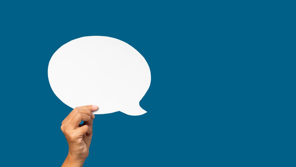 Hand holding of an empty white speech bubble over blue background. Speech bubble balloon concept.